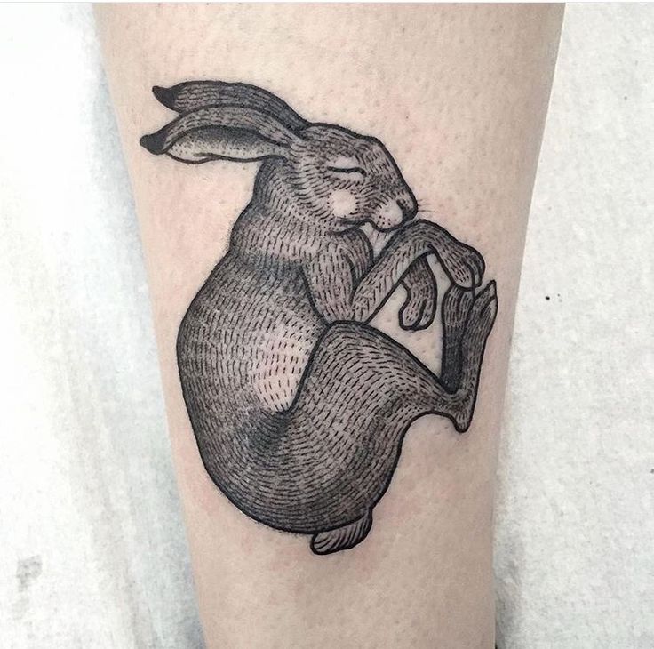 a black and white tattoo of a rabbit holding a piece of paper in its paws