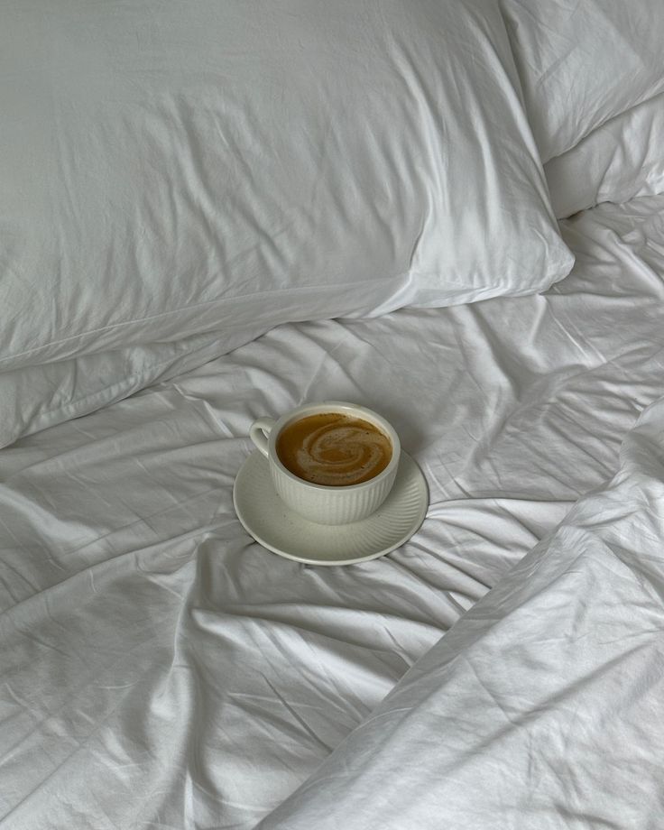 a cup of coffee sitting on top of a white bed