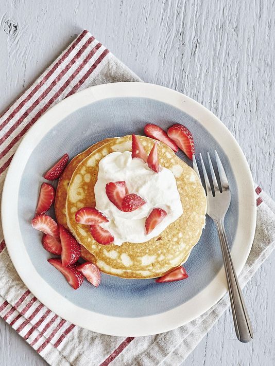 a white plate topped with pancakes covered in whipped cream and sliced strawberries next to a fork