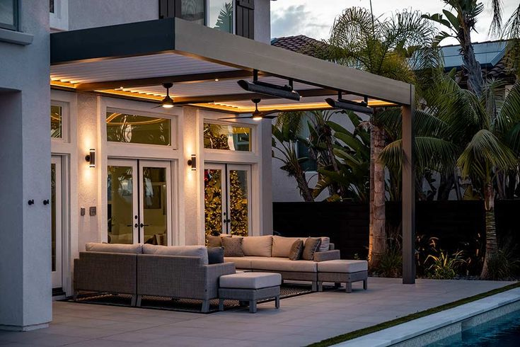 an outdoor living area with couches and chairs next to a swimming pool at dusk