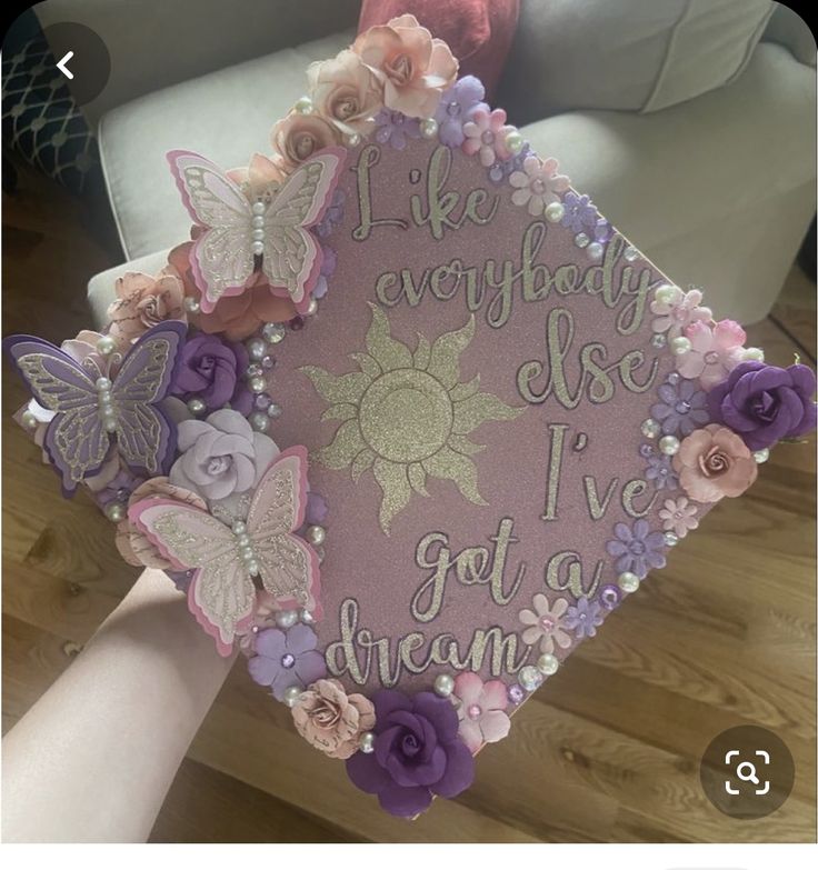 someone is holding up a graduation cap decorated with flowers and butterfly decorations that read, i like anybody else i've got to dream