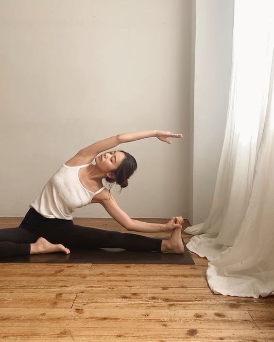 a woman is doing yoga in front of a white curtain with her arms stretched out