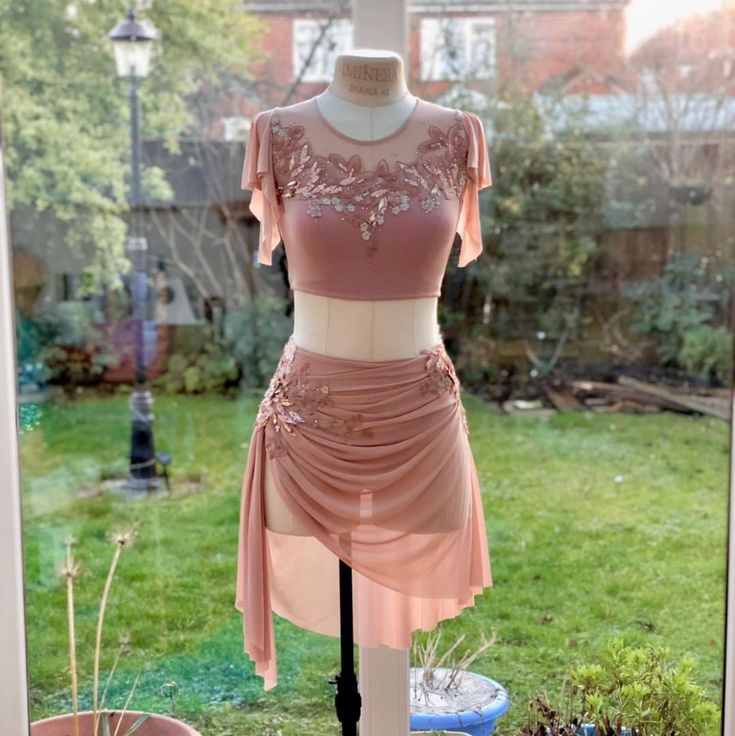 a dress on display in front of a window with grass and bushes behind the mannequin