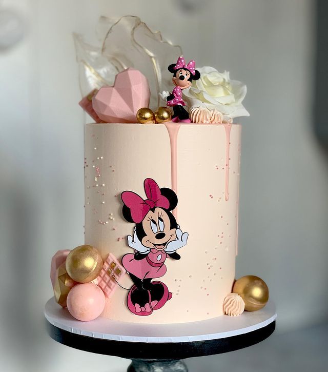 a pink and gold cake decorated with minnie mouse figurines