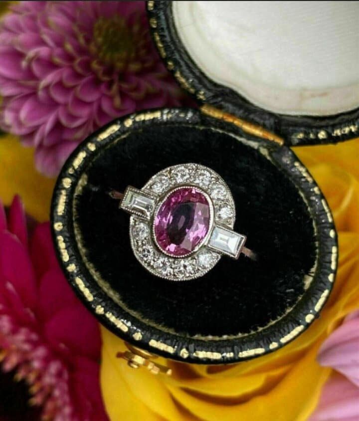 an oval shaped pink stone ring in a black velvet box with gold trimmings