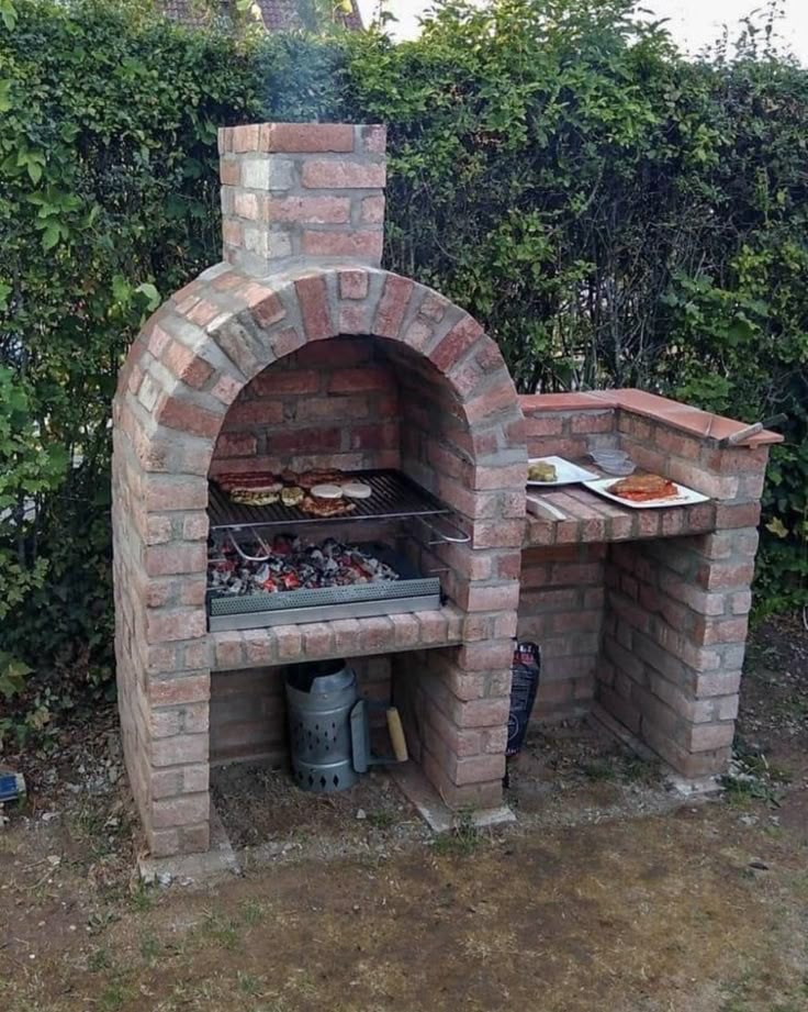 an outdoor brick pizza oven in the middle of some bushes and trees with food cooking on it