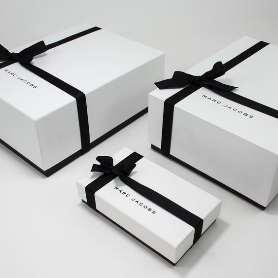 three white boxes with black ribbons and bows on them, one has a logo on the front