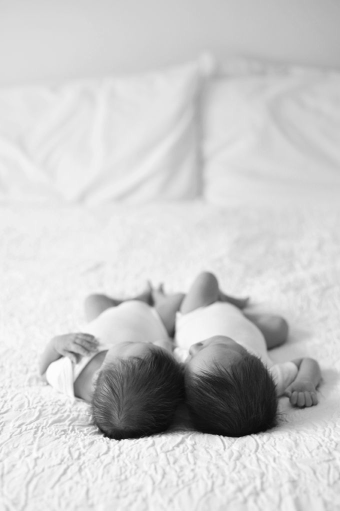 two babies laying on top of each other on a bed