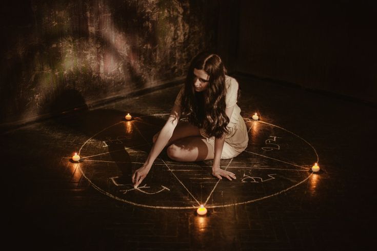 a woman sitting in the middle of a circle with candles around her and writing on it