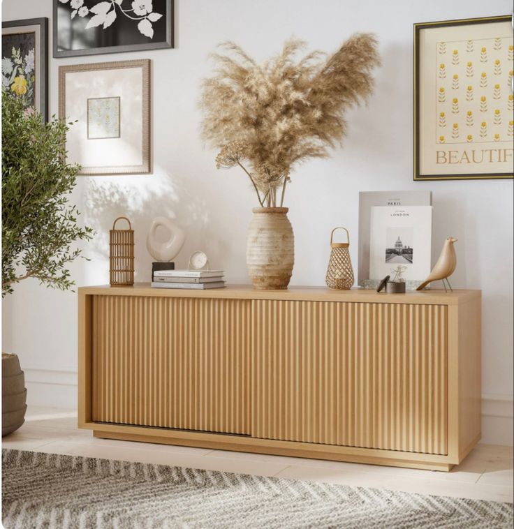 a vase filled with dry grass sitting on top of a wooden dresser next to pictures