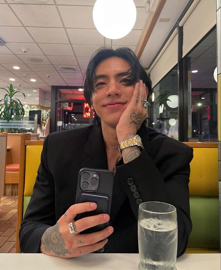 a man sitting at a table with a cell phone in his hand and a glass of water next to him