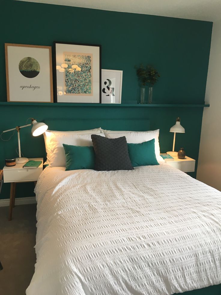 a bedroom with green walls and white bedspread, two framed pictures on the wall