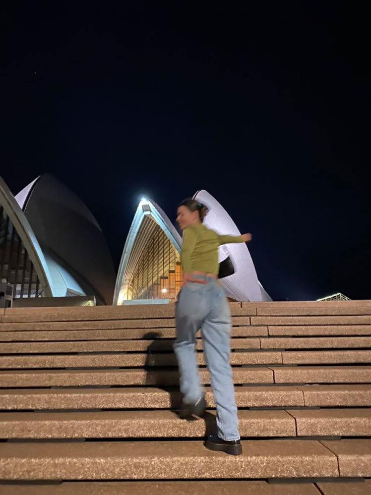 a woman is walking up some steps in front of the sydney opera house at night