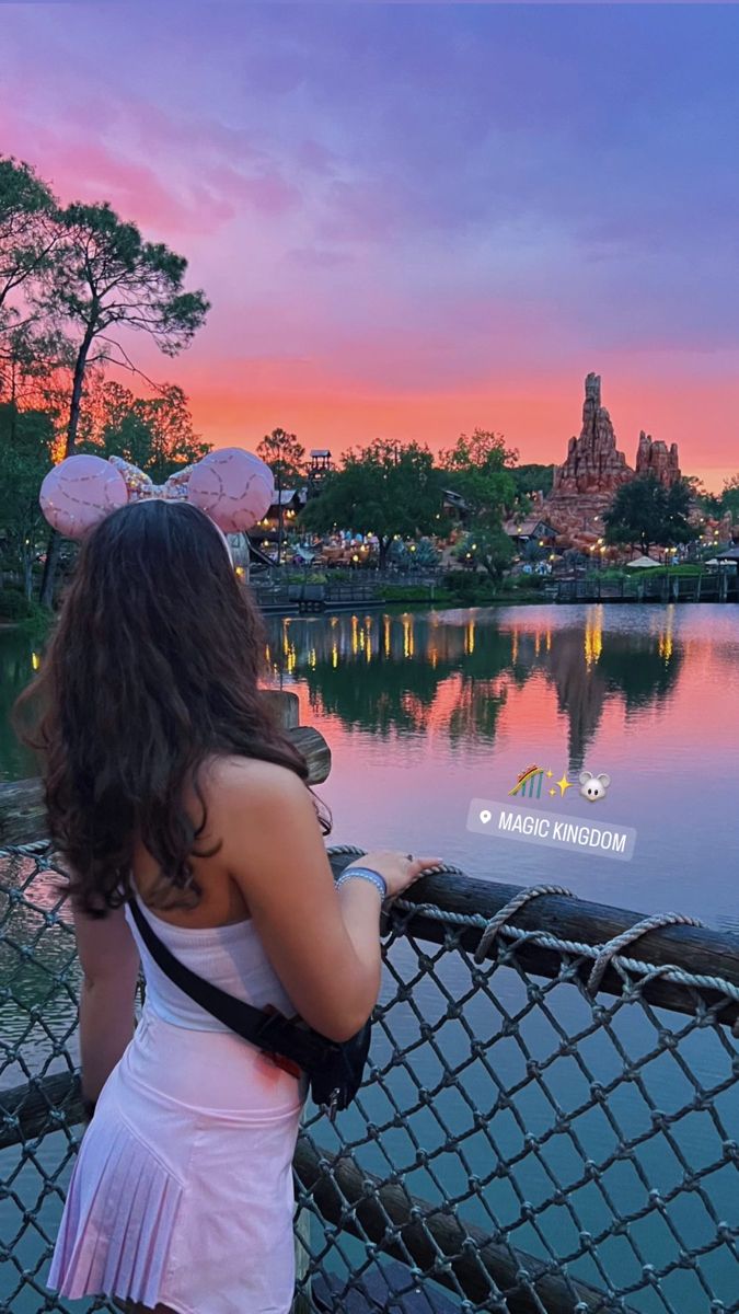 a woman standing on top of a bridge next to a body of water at sunset