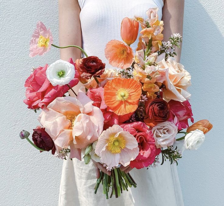 a woman holding a large bouquet of flowers in her hands and wearing a white dress