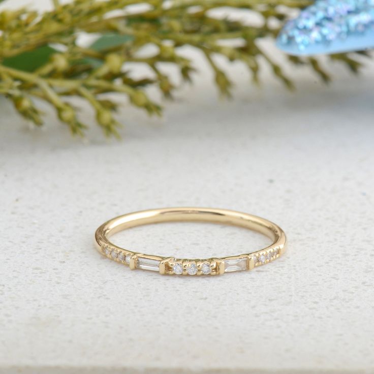 a yellow gold ring with five small diamonds on the side, sitting next to a plant