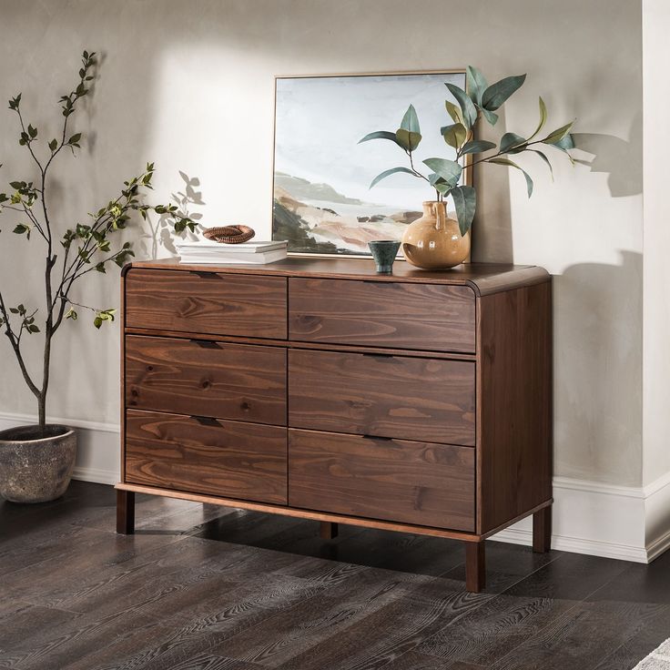 a wooden dresser sitting next to a potted plant on top of a hard wood floor