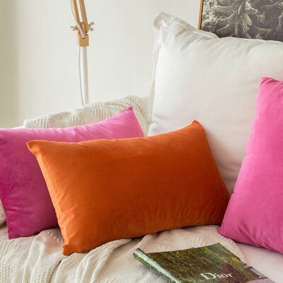 four different colored pillows sitting on top of a bed next to a book and lamp