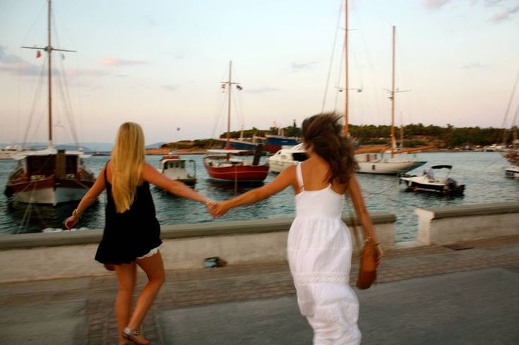 two women holding hands while walking near boats