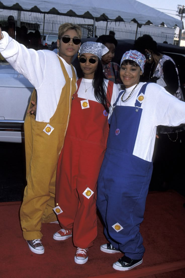 three people standing next to each other with their arms in the air and one person wearing overalls