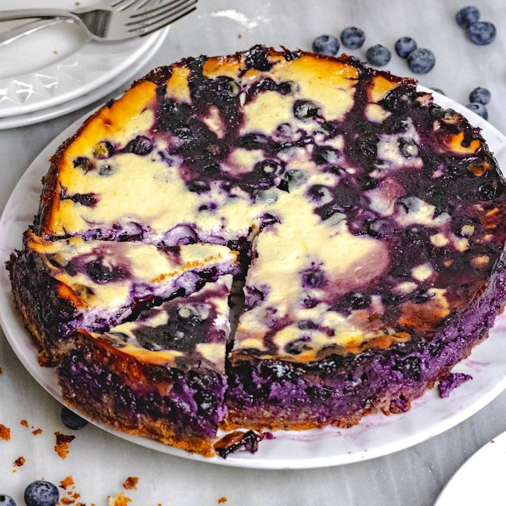 a blueberry cheesecake is cut into slices on a white plate with silverware