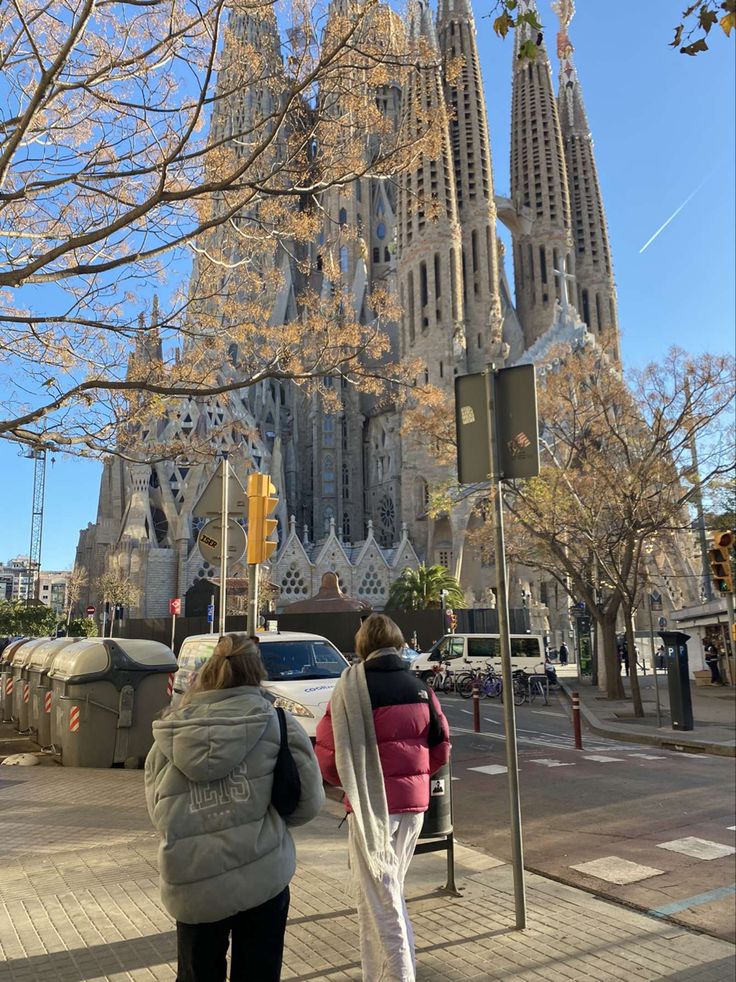 two people walking down the sidewalk in front of a cathedral