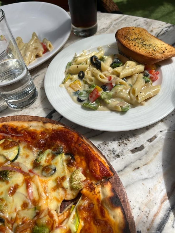 a table topped with plates of food next to glasses of water and pizza on top of it