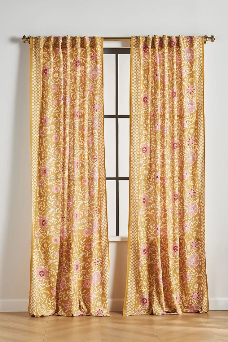 an open window with yellow curtains and pink flowers on the drapes, in front of a white wall