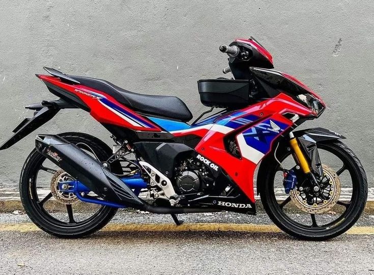 a red, white and blue motorcycle parked in front of a gray wall with graffiti on it