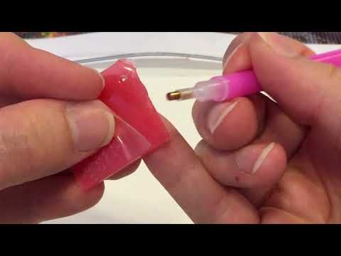 two hands holding pink pens and writing on a piece of clear plastic with gold tips