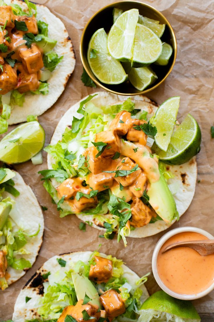 three tacos with chicken, lettuce and avocado next to dipping sauce