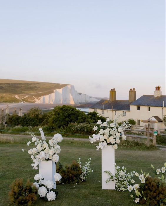 two white vases filled with flowers sitting on top of a lush green field next to the ocean