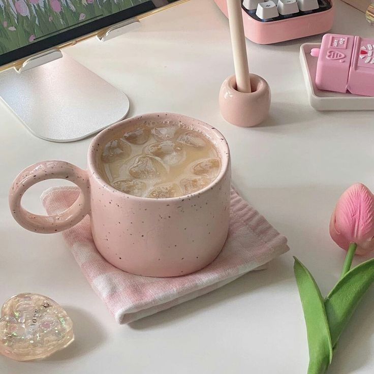 a pink coffee cup sitting on top of a white table next to a pink flower