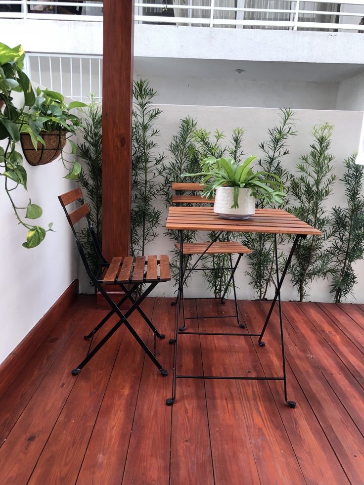 two chairs and a table on a wooden floor next to a balcony with potted plants