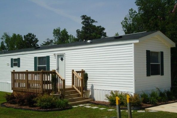 a mobile home sits in the grass next to a wooden deck and steps leading up to it's front door