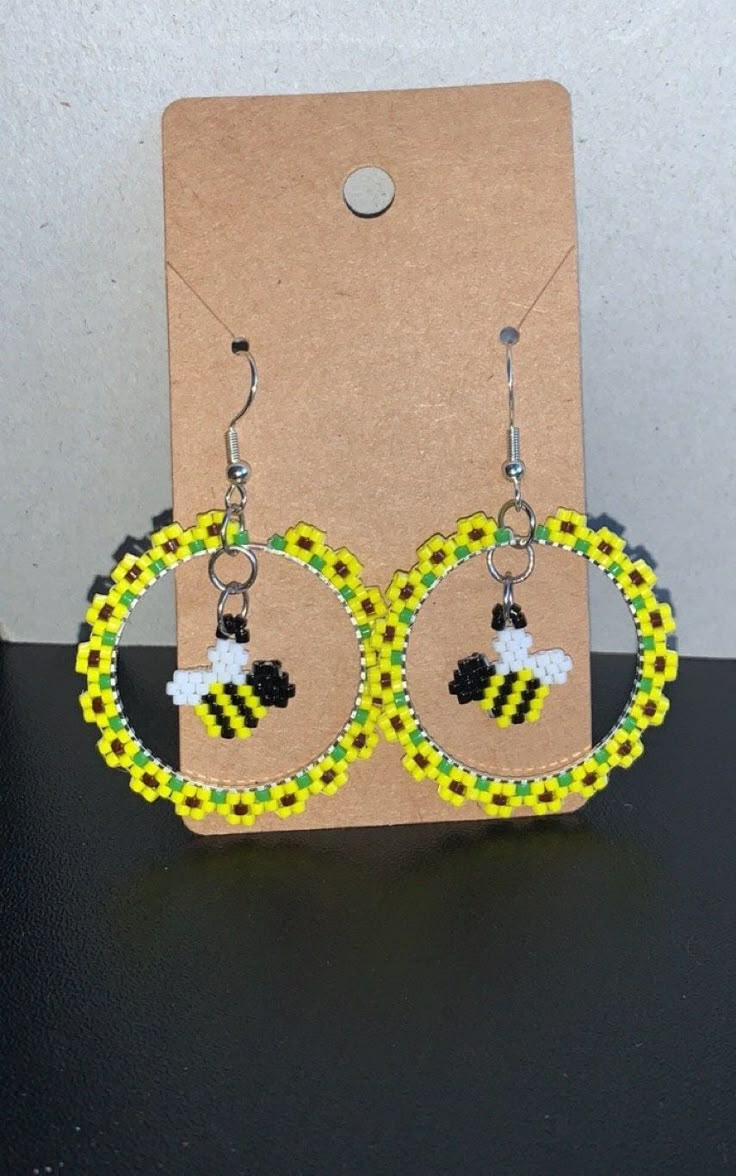 a pair of yellow and black beaded bee hoop earrings on a brown card board