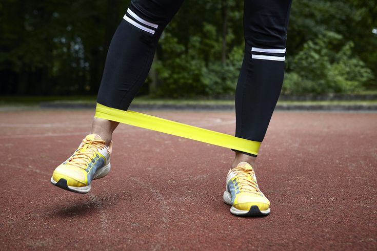 a person standing on a tennis court holding a yellow tape around their ankles and feet