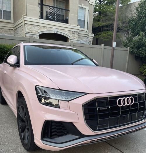 a pink audi suv parked in front of a house on a street with trees and bushes