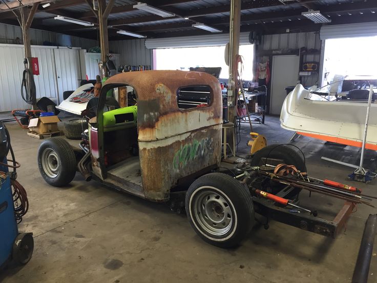 an old rusty truck in a garage with other vehicles and tools on the ground next to it