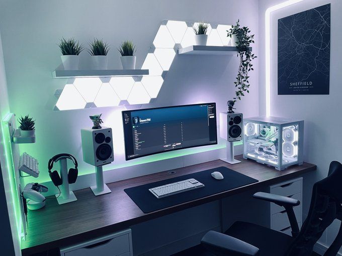 a computer desk topped with a monitor and speakers next to a plant on top of a shelf