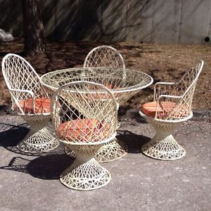 four white wicker chairs and table with orange cushions on concrete ground next to tree