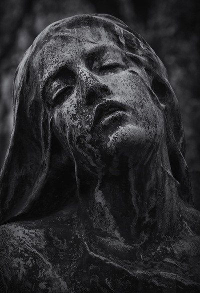 a black and white photo of a woman's face covered in mud, with trees in the background