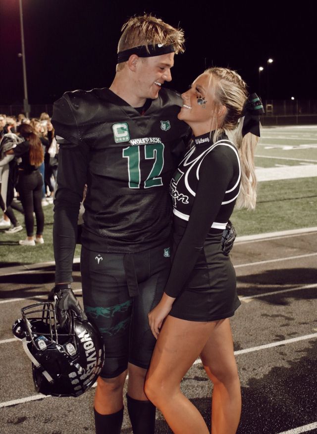 a man and woman in football uniforms standing next to each other on a field at night