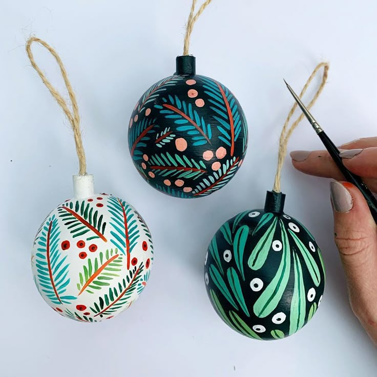 three hand painted ornaments are being held by someone's hands with scissors on the table