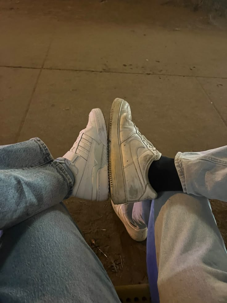 two people are sitting on the curb with their feet up and one is wearing white sneakers