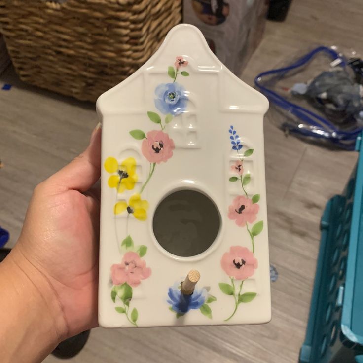 a person holding up a white birdhouse with flowers painted on the front and sides