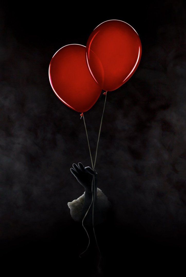 a person holding two red balloons in the dark