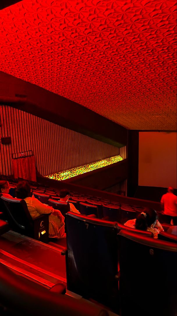 an auditorium with red lighting and people sitting in the seats