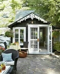 a small black and white shed with patio furniture in the front yard, surrounded by trees