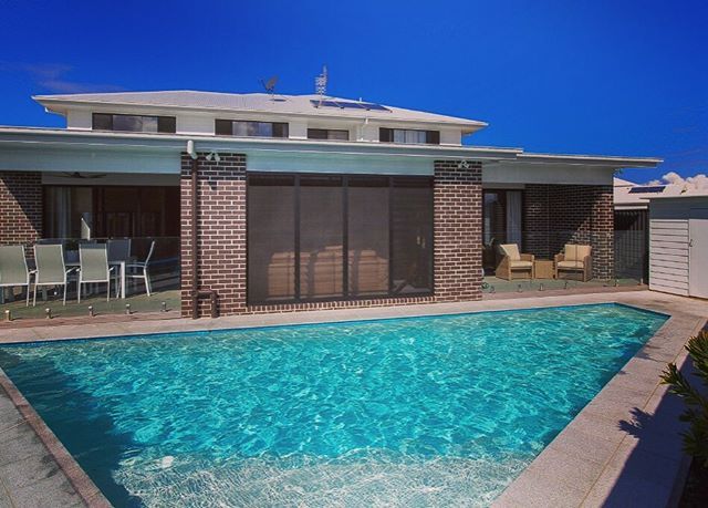 an empty swimming pool in front of a brick house with patio furniture and sliding glass doors